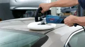 Una persona pule el techo de un automóvil con una pulidora eléctrica en un taller.