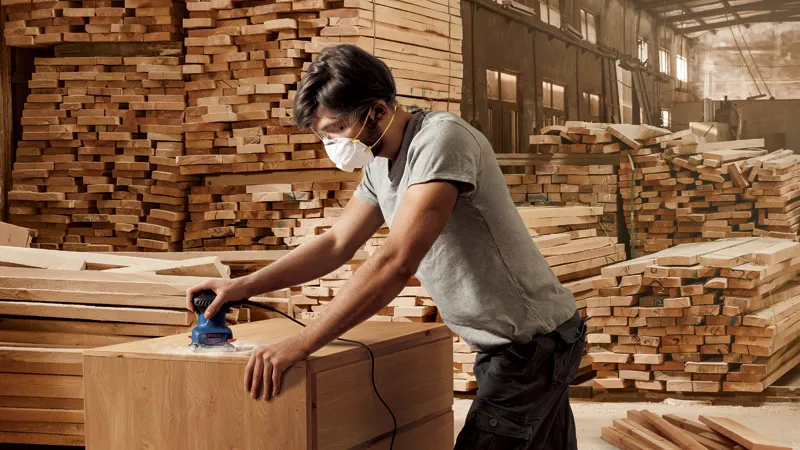 Hombre lijando madera, con máscara.