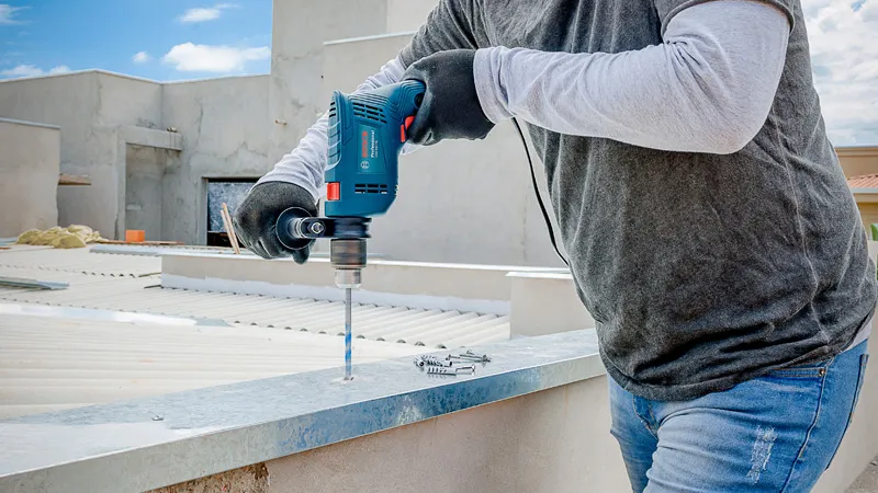 Una persona que usa equipo de seguridad perfora metal en un tejado utilizando un taladro de impacto.