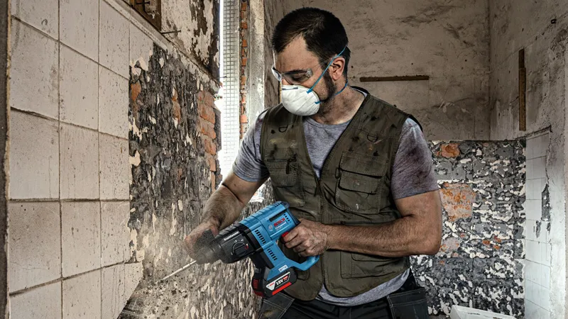 Una persona que usa equipo de seguridad quita azulejos de una pared usando una herramienta eléctrica.