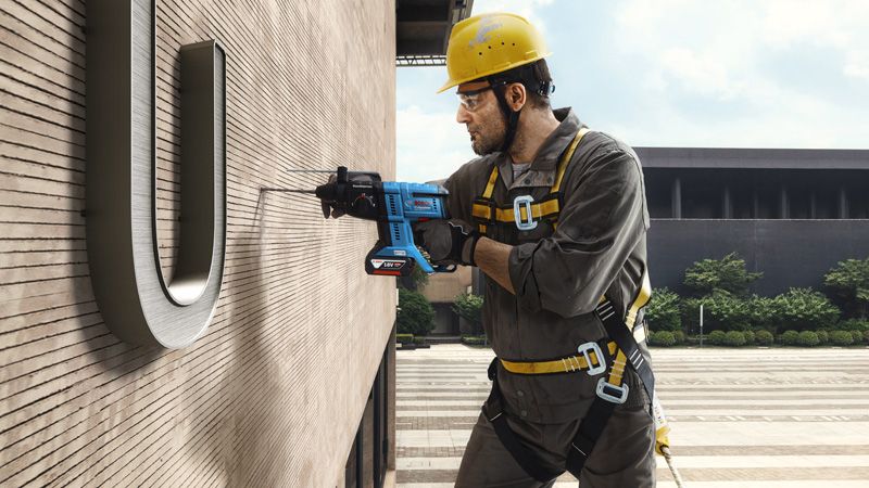 Una persona que usa equipo de seguridad perfora la pared de un edificio mientras está suspendida.