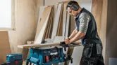 Una persona que usa equipo de seguridad corta madera en una sierra de mesa en un taller.