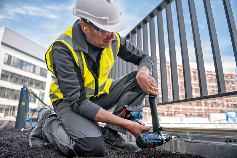 Una persona que usa equipo de seguridad utiliza un taladro combinado inalámbrico en el marco de una cerca de metal.