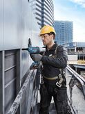 Una persona que usa equipo de seguridad perfora un panel metálico en el exterior de un edificio.