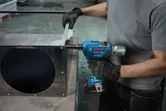Una persona que usa equipo de seguridad utiliza una llave de impacto inalámbrica en un conducto de metal.