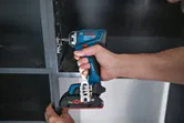 Una persona utiliza un taladro/destornillador inalámbrico para fijar una bisagra de armario.