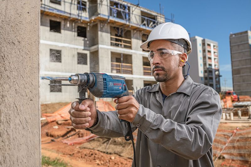 Una persona que usa equipo de seguridad perfora una pared de hormigón en un sitio de construcción.