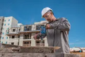 Una persona que usa equipo de seguridad utiliza un taladro de impacto en un sitio de construcción.