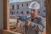 Una persona que usa equipo de seguridad perfora madera en un sitio de construcción.