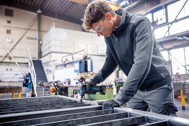 Una persona que usa equipo de seguridad utiliza una amoladora rotatoria sobre un marco de metal.