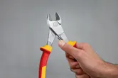Una persona sostiene unos alicates de corte lateral diagonal aislados con mangos rojos y amarillos.