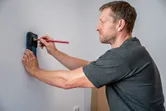 Persona marcando una pared con un lápiz mientras utiliza un detector electrónico.