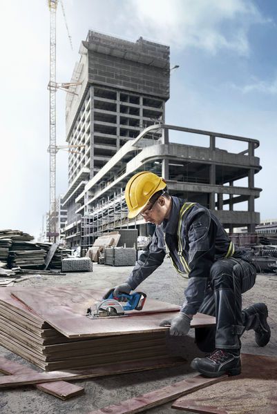 Una persona que usa equipo de seguridad corta madera contrachapada apilada en un sitio de construcción.