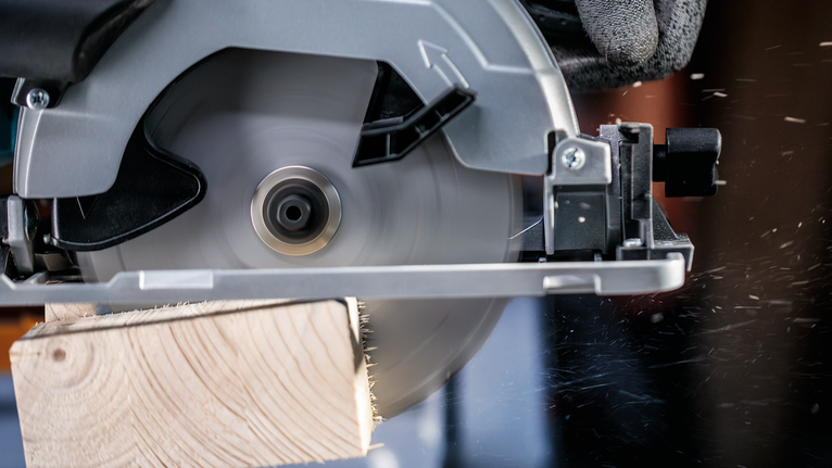 Una persona que usa equipo de seguridad corta una tabla de madera con una sierra circular.