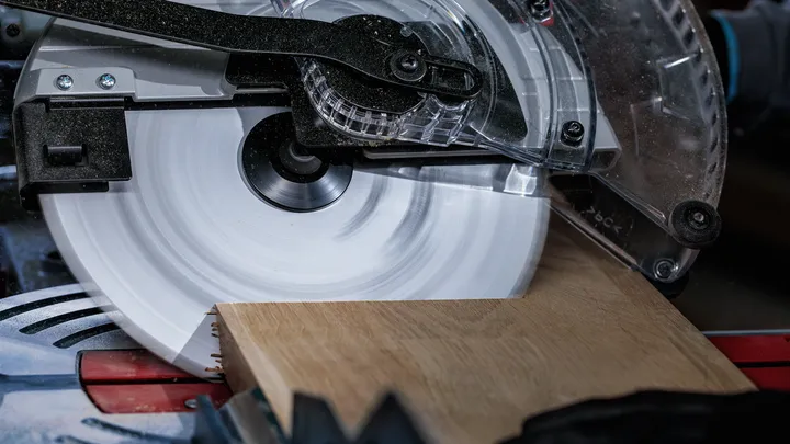 Persona que usa equipo de seguridad corta una tabla de madera con una sierra circular.