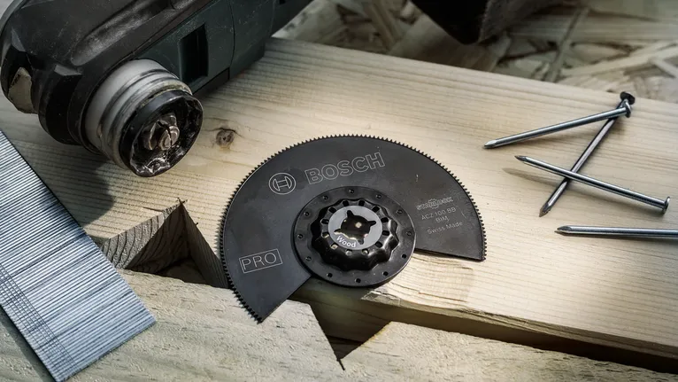 Accesorio de hoja de sierra circular para cortar madera colocado sobre una tabla de madera con clavos cerca.