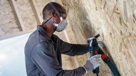 Una persona que usa equipo de seguridad perfora un agujero rectangular en una pared de madera.