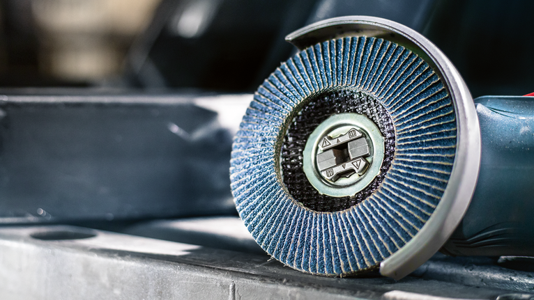 Un primer plano de una amoladora de disco de láminas azul apoyada sobre una superficie metálica.