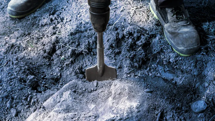 Una persona que usa equipo de seguridad utiliza una herramienta de demolición para romper suelo duro.