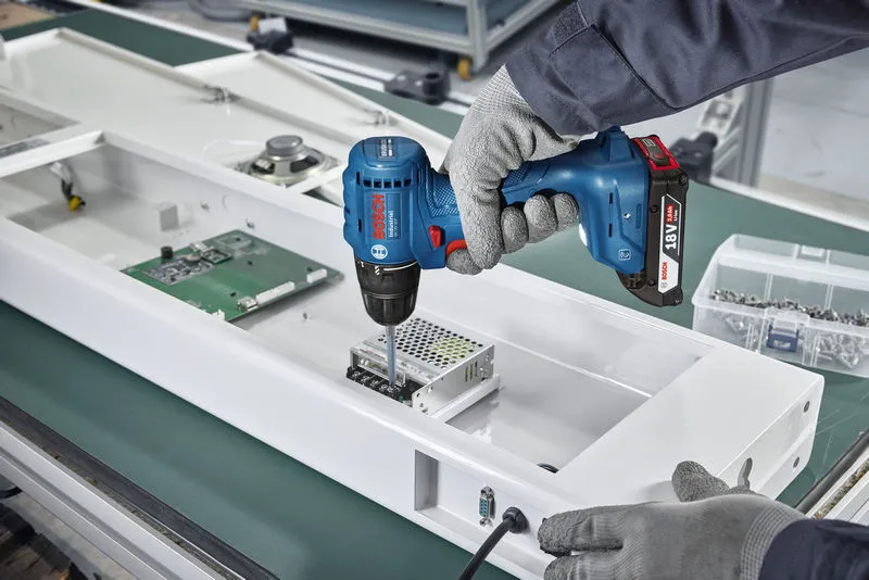 Una persona que usa equipo de seguridad utiliza un taladro inalámbrico para ensamblar componentes electrónicos.