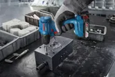 Una persona que usa equipo de seguridad utiliza un taladro inalámbrico para fijar un tornillo en el metal.
