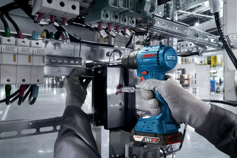 Una persona que usa equipo de seguridad utiliza un taladro inalámbrico en un panel eléctrico.