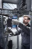 Una persona que usa equipo de seguridad utiliza un taladro inalámbrico dentro de un armario eléctrico.
