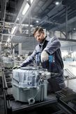 Una persona que usa equipo de seguridad utiliza un taladro inalámbrico para ensamblar maquinaria en una fábrica.