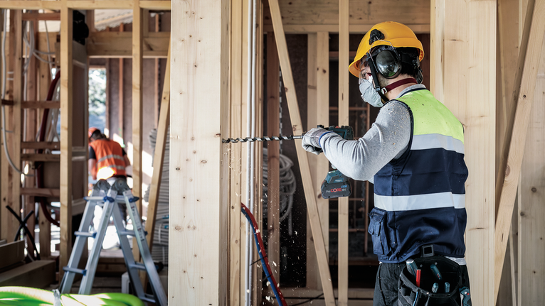 Una persona que usa equipo de seguridad perfora un marco de madera en un sitio de construcción.