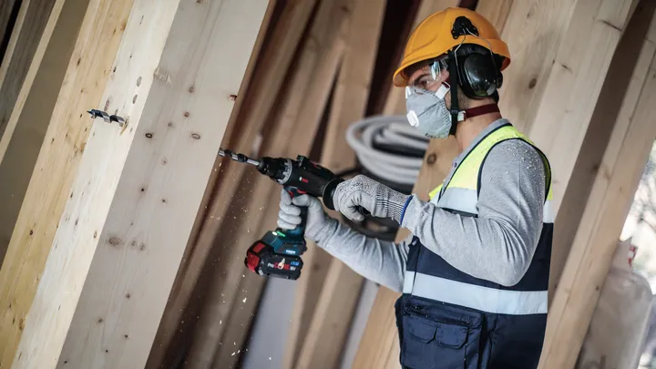 Persona que usa equipo de seguridad perfora una viga de madera.