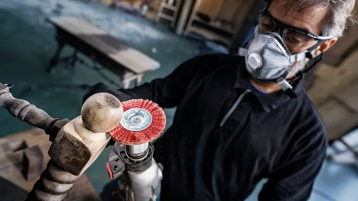 Una persona que usa equipo de seguridad pule un huso de madera con una herramienta eléctrica.