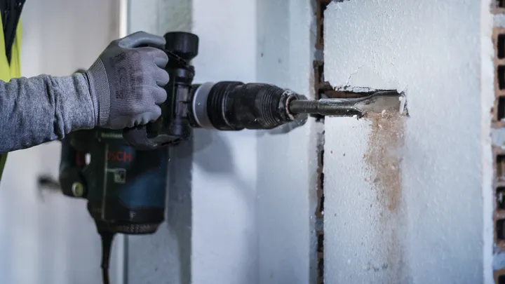 Una persona que usa equipo de seguridad utiliza un martillo rotatorio para cincelar una ranura rectangular en una pared.