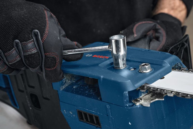 Una persona que usa equipo de seguridad ajusta una motosierra inalámbrica con una llave.