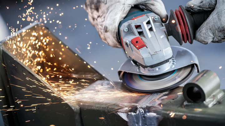 Una persona que usa equipo de seguridad muele metal, produciendo chispas brillantes.