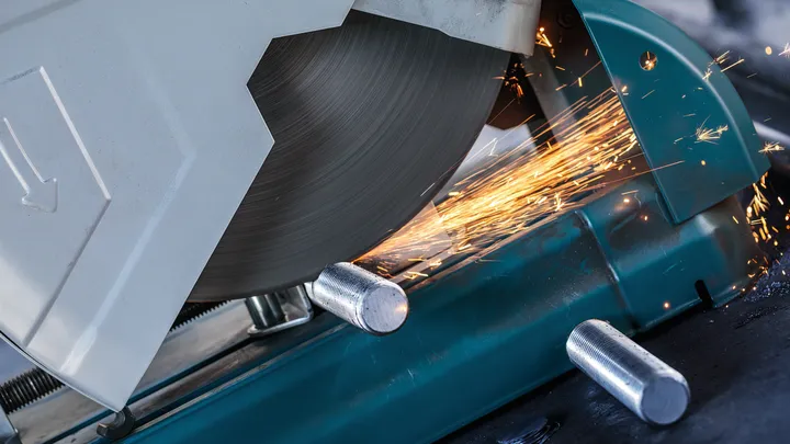 Sierra de corte de metal cortando una varilla de acero mientras saltan chispas.