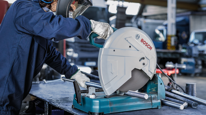 Una persona que usa equipo de seguridad opera una sierra circular para cortar tubos de metal.