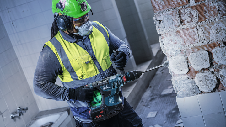 Una persona que usa equipo de seguridad perfora una pared de ladrillos en un área de construcción.