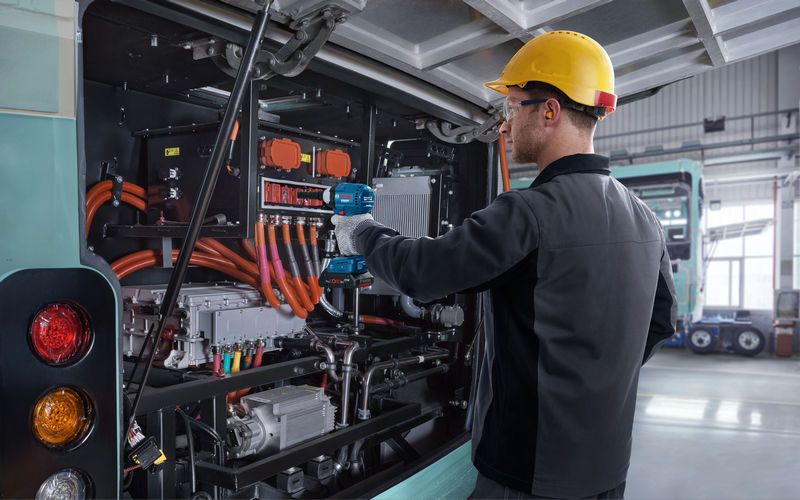 Una persona que usa equipo de seguridad utiliza una llave de impacto en el motor de un autobús eléctrico.