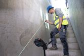Una persona que usa equipo de seguridad marca una pared usando una herramienta niveladora láser en las escaleras.