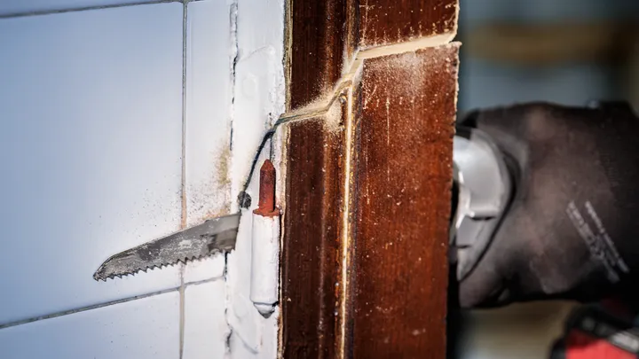 Persona que usa equipo de seguridad y utiliza una herramienta eléctrica para cortar un marco de puerta de madera.