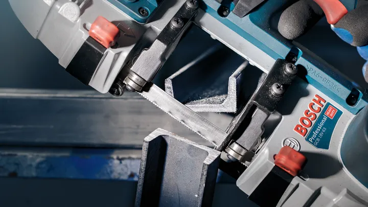 Una persona que usa equipo de seguridad utiliza una sierra eléctrica para cortar una viga de metal.