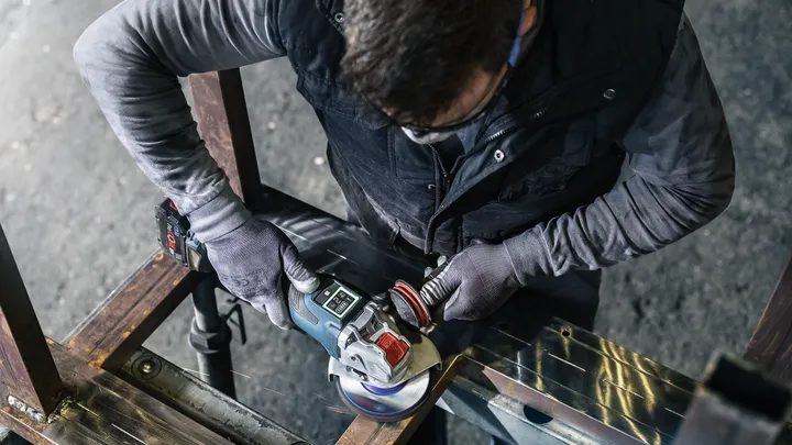 Una persona que usa equipo de seguridad muele metal con una amoladora angular.