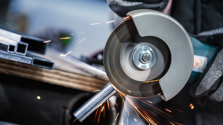 Una persona que usa equipo de seguridad utiliza una amoladora angular para cortar un tubo de metal.