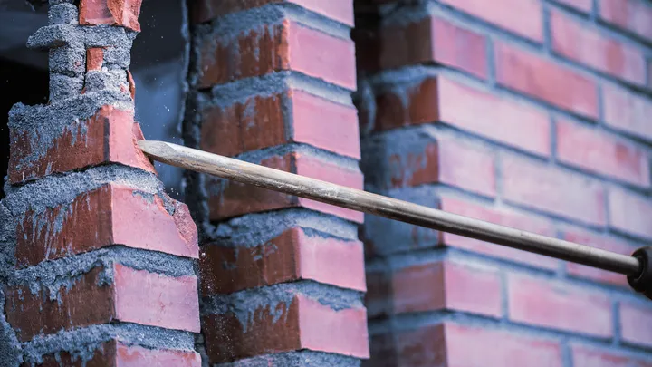 Herramienta de cincel rompiendo una pared de ladrillos rojos.