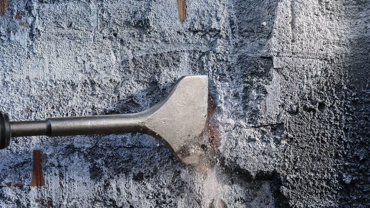 Una broca de cincel quita hormigón de una superficie de pared rugosa.