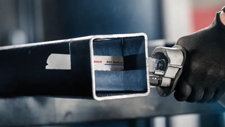 Una persona que usa equipo de seguridad corta un tubo de metal con una sierra alternativa.