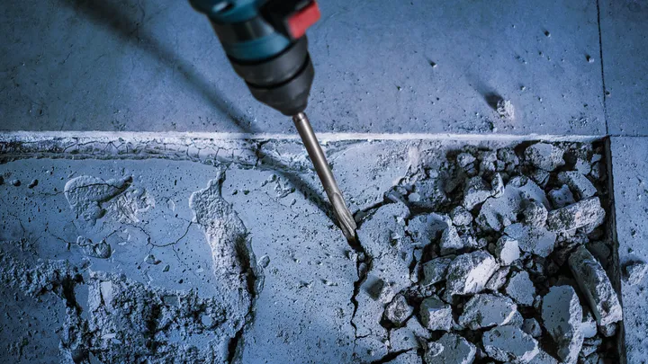 Martillo rotatorio rompiendo una superficie de piso de baldosas con escombros dispersos.