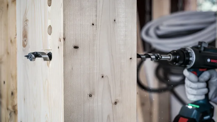 Una persona que usa equipo de seguridad utiliza un taladro eléctrico para perforar una viga de madera.