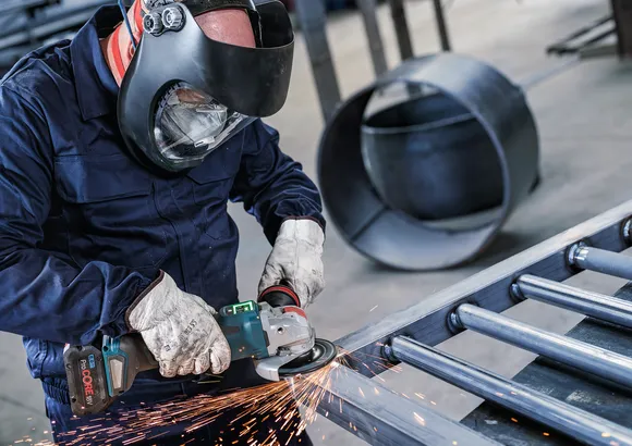 Persona que usa equipo de seguridad muele vigas de metal, creando chispas.