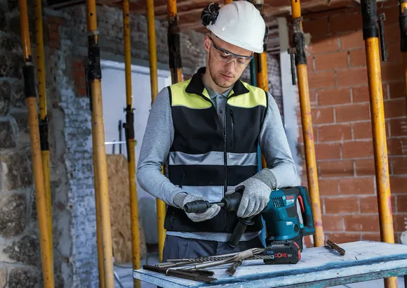 Una persona que usa equipo de seguridad prepara un martillo perforador en un sitio de construcción.